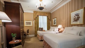 Ein Hotelzimmer mit zwei Betten, einer Chandelieber, einem Schreibtisch mit Lampe und einem Sessel.