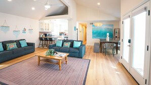 A spacious living area with a dark grey sofa, a wooden coffee table, and a large painting of a wave on the wall. - 2 Car Garage Parking, AC, Kid Friendly, 45 seconds from the beach! (San Diego)