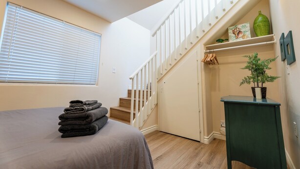 A bedroom with a bed, a staircase, a wall-mounted shelf with decorative items, and a potted plant. - 2 Car Garage Parking, AC, Kid Friendly, 45 seconds from the beach! (San Diego)