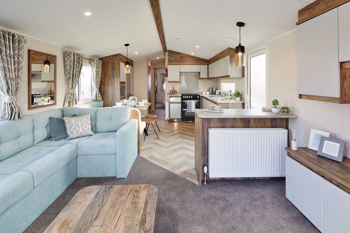 Een moderne woonkamer met een modulaire bank, een houten salontafel, en een keukenhoek met fornuis en kasten.