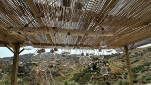 Uma pérgola de madeira com lâmpadas penduradas e vista para uma paisagem ondulada.
