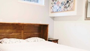 A bedroom with a wooden headboard, a white bedspread, a bench, a small bedside table, and a window with blinds. - Ideal for long stays, Near/airport GYM-Parking. (Toronto)