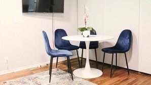 A room with a white round table, four blue chairs, a potted orchid, and a flat-screen TV mounted on the wall. - Ideal for long stays, Near/airport GYM-Parking. (Toronto)