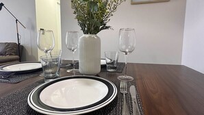 A dining table set with plates, cutlery, and glasses, a vase with greenery, and framed artwork on the wall. - Vista Laguna Oriente By Andes+ (Concepción)