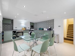 Une cuisine moderne avec une table et des chaises en verre, un four à micro-ondes et un lave-linge.