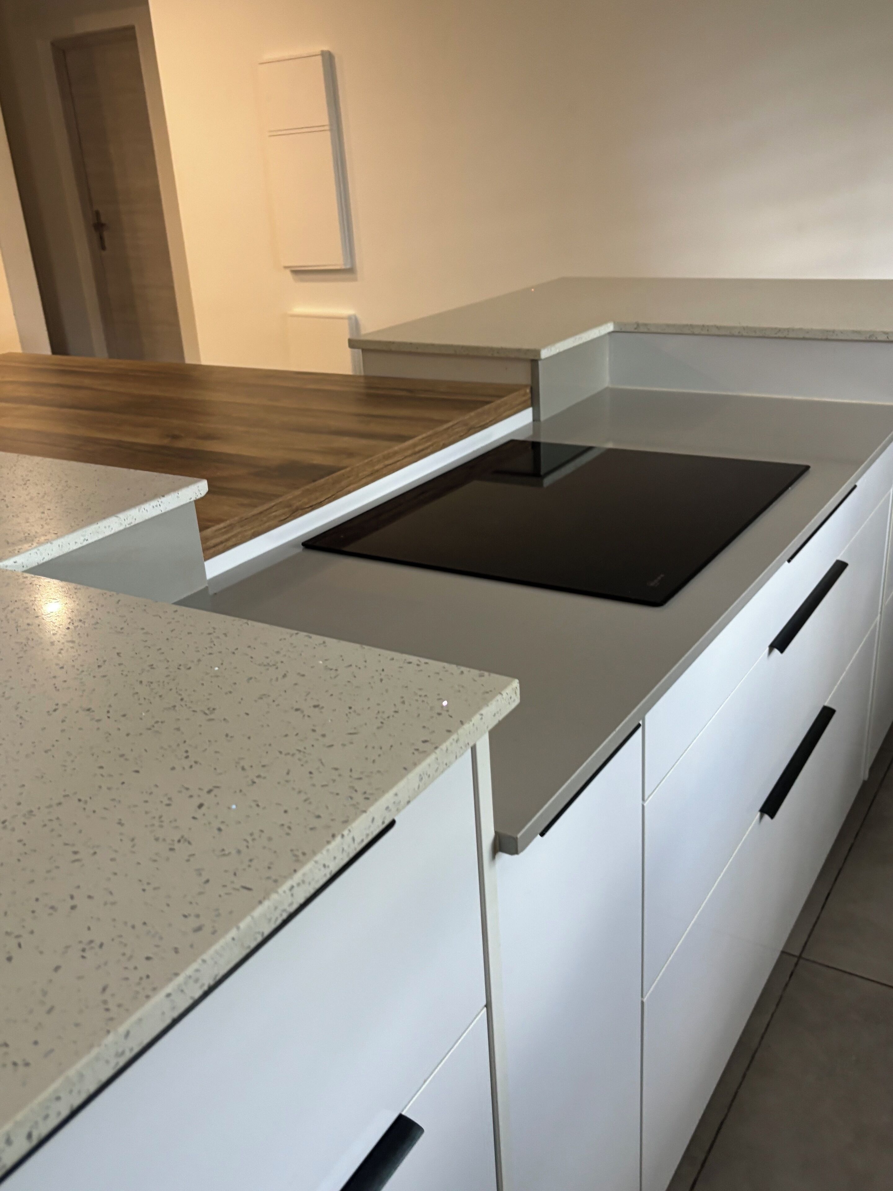 Una cucina moderna con mobili bianchi, un piano di lavoro maculato e un piano cottura a induzione nero.