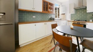 A modern kitchen with white cabinets, a green-tiled backsplash, a wooden countertop, and a round dining table with chairs. - Pass the Keys | Cosy apartment in Kilburn (London)