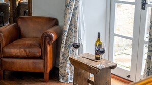 A leather armchair, a wooden side table with a wine bottle and glass, and a window with curtains. - Pass the Keys | Cotswold Country Style Living | Chipping Norton (Chipping Norton)