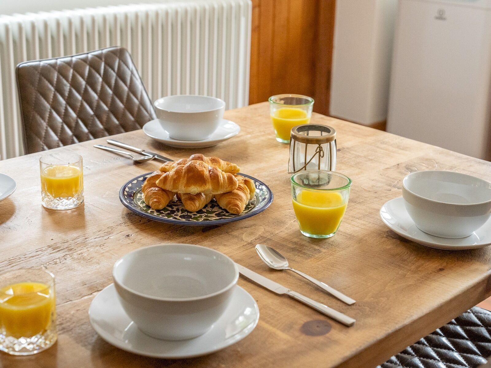 Desayuno con cruasanes, zumo de naranja y cuencos blancos sobre una mesa de madera.