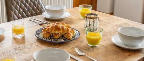 Desayuno con cruasanes, zumo de naranja y cuencos blancos sobre una mesa de madera.