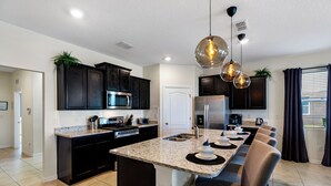 A modern kitchen with dark cabinetry, a granite countertop, and a central island with seating. - Solterra- LakeView - Private Pool & Spa  (Davenport)