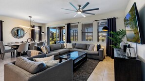 A modern living room with a sectional sofa, a glass coffee table, and a dining area with chairs and a table. - Solterra- LakeView - Private Pool & Spa  (Davenport)