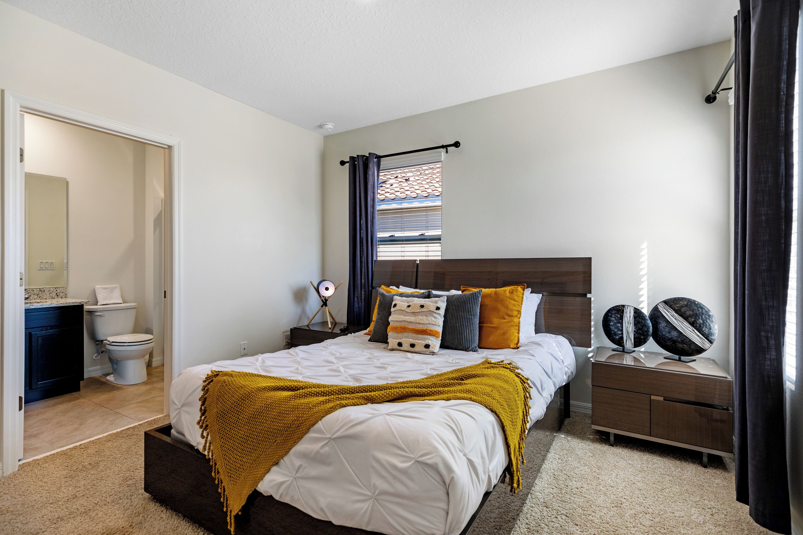 Un dormitorio con cama, mesita de noche y ventana con cortinas.