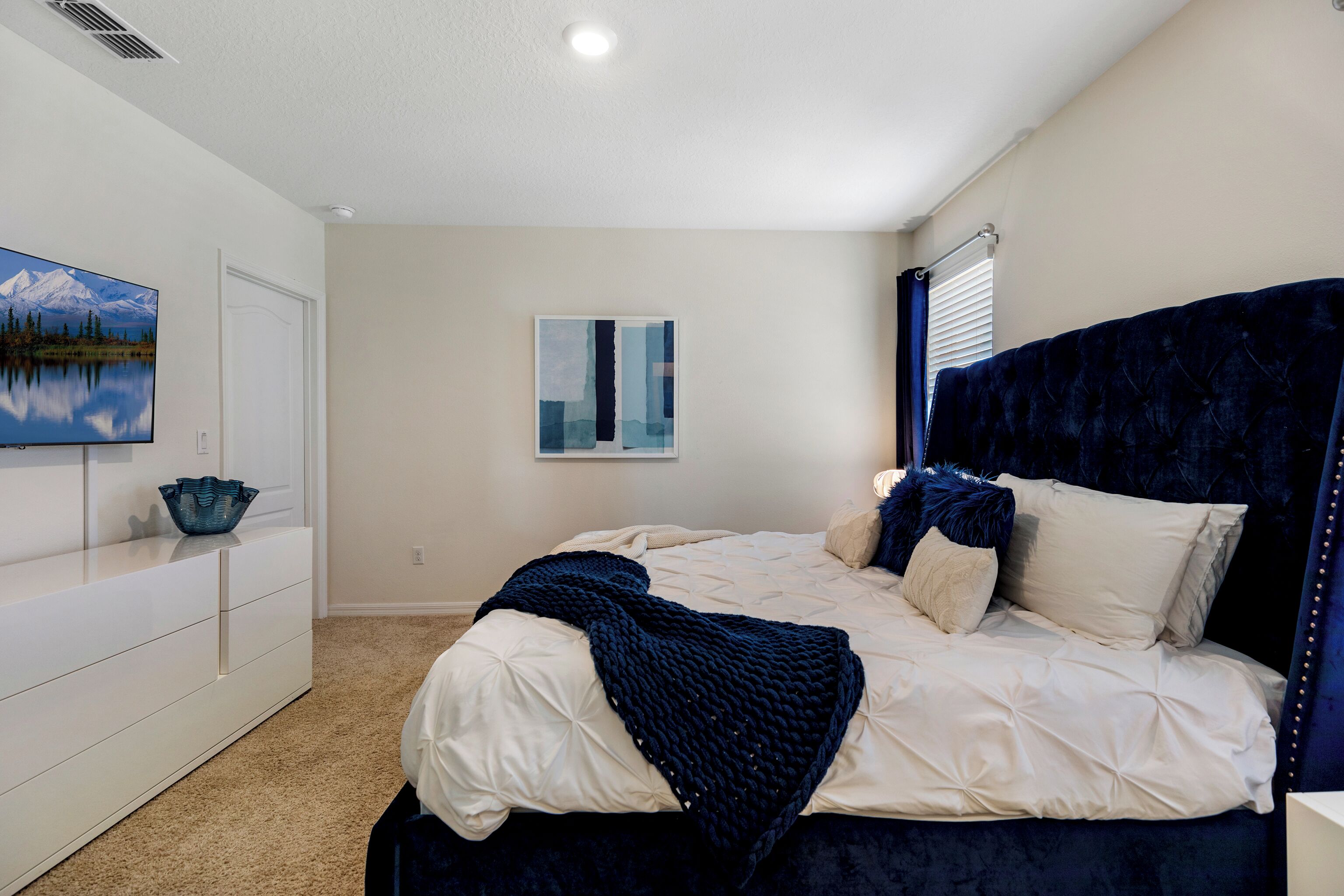 A bedroom with a bed, a dresser, a painting, and a window with blinds.