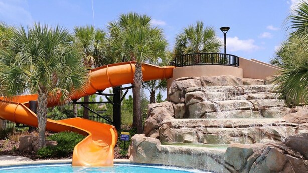 A pool with two orange slides, a rock waterfall, and palm trees. - Solterra- LakeView - Private Pool & Spa  (Davenport)