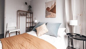 A neatly arranged bedroom with a bed, bedside tables, a hanging abstract artwork, and a chair. - Pacific Sun CBD Apartment (Yamba)