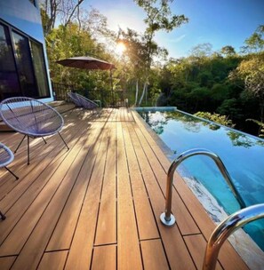 Un patio in legno con piscina, immerso tra alberi e affiancato da un edificio moderno.