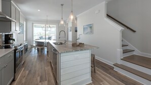 Une cuisine moderne dotée d’un îlot central, d’appareils électroménagers en acier inoxydable et de luminaires suspendus.