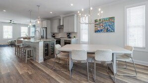 Une cuisine moderne dotée d’un grand îlot central, d’appareils électroménagers en acier inoxydable et d’un coin repas avec une table et des chaises blanches.
