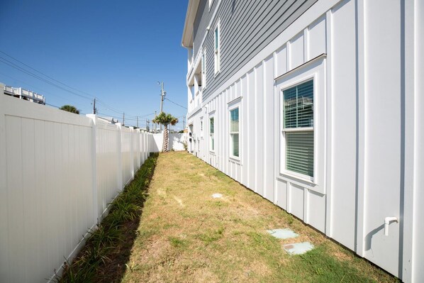 A narrow, grassy pathway flanked by white fences and a building with multiple windows and a door.