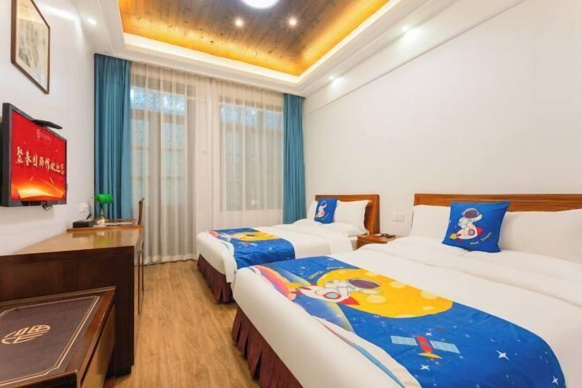 Habitación de hotel con dos camas, un escritorio, una silla, una ventana con cortinas e iluminación empotrada en el techo.