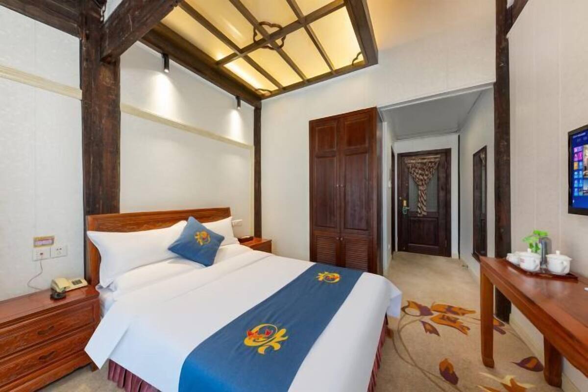Una habitación de hotel con una cama de madera, una mesita de noche con teléfono, un escritorio con una planta y un armario.