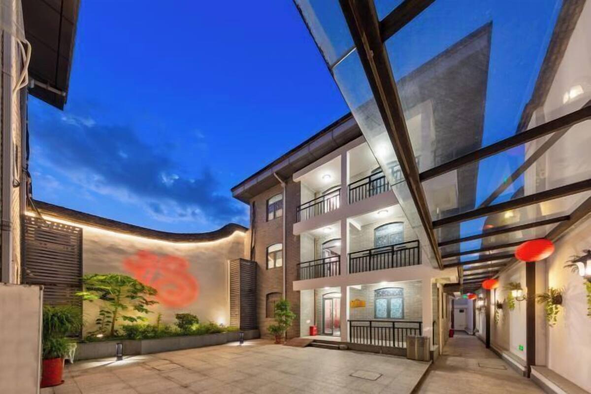 Un edificio moderno con fachada de vidrio, un patio con plantas y una entrada visible.