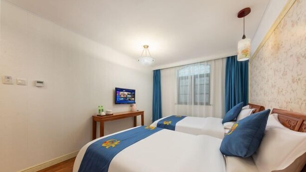 Ein Hotelzimmer mit zwei Betten, einem Fernseher, einem kleinen Tisch und einem Fenster mit Vorhängen.