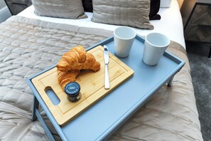 A bed with a quilted blanket, a wooden tray with a croissant, a knife, and two cups.