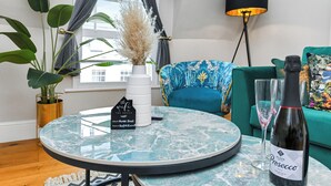 A modern living room with a round glass table, a green sofa, a potted plant, a vase with dried flowers, a wine bottle, and a lamp. - Market Street Apartment 3A Flat 4 (Nottingham)