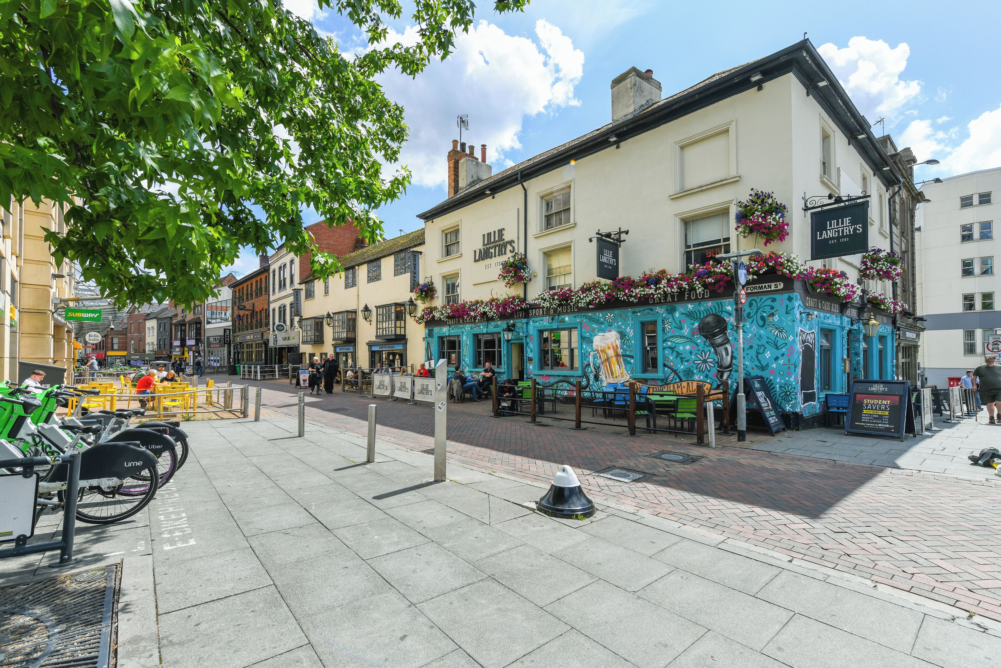 A street with a pub named 'Lillie Langtry's' featuring outdoor seating and flower baskets.