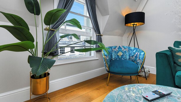 A room with a large window, a blue chair, a green sofa, a floor lamp, and a table with a remote control. - Market Street Apartment 3A Flat 4 (Nottingham)