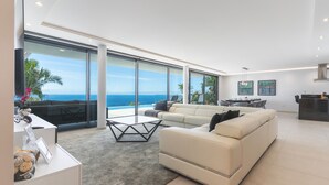 A modern living room with a large sofa, a coffee table, and a view of the ocean.