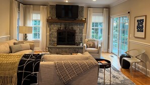 A living room with a stone fireplace, a large flat-screen TV, a sofa, and a chair. - Luxury 5BR retreat w/3rd floor sleeps 26 adults; 1 mile to town; 1 month min (Ridgefield)