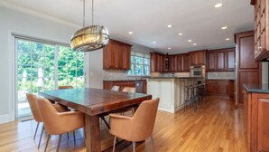 A spacious kitchen with wooden cabinets, a dining table with chairs, and a large window providing a view of greenery outside. - Luxury 5BR retreat w/3rd floor sleeps 26 adults; 1 mile to town; 1 month min (Ridgefield)