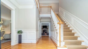 A spacious hallway with wooden flooring, a staircase with white railings and wooden steps, and a view into another room with a fireplace. - Luxury 5BR retreat w/3rd floor sleeps 26 adults; 1 mile to town; 1 month min (Ridgefield)