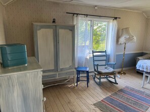 A room with a wooden floor, a wardrobe, a rocking chair, a small table, and a bed with a patterned bedspread. - 2 Person Holiday Home in Farentuna (Faerentuna)