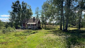 A red wooden house with a porch, surrounded by trees and a grassy field.