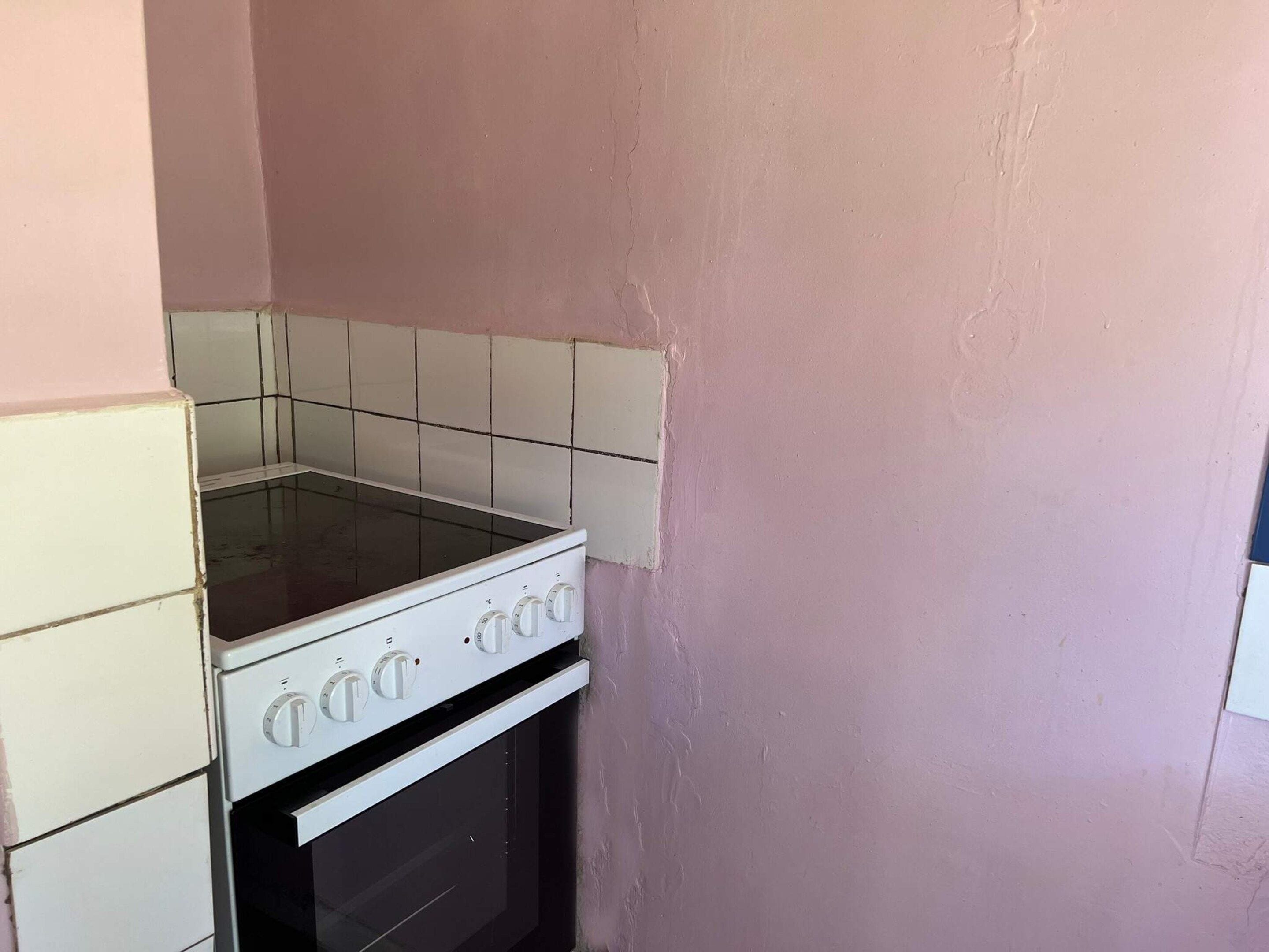 Une petite cuisine avec un four blanc, une cuisinière blanche et un pare-feu en carreaux.