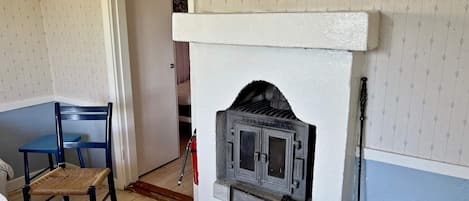 A room with a fireplace, a blue chair, a white bucket, and a door leading to another room.