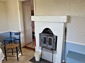 A room with a fireplace, a blue chair, a white bucket, and a door leading to another room. - 2 Person Holiday Home in Farentuna (Faerentuna)