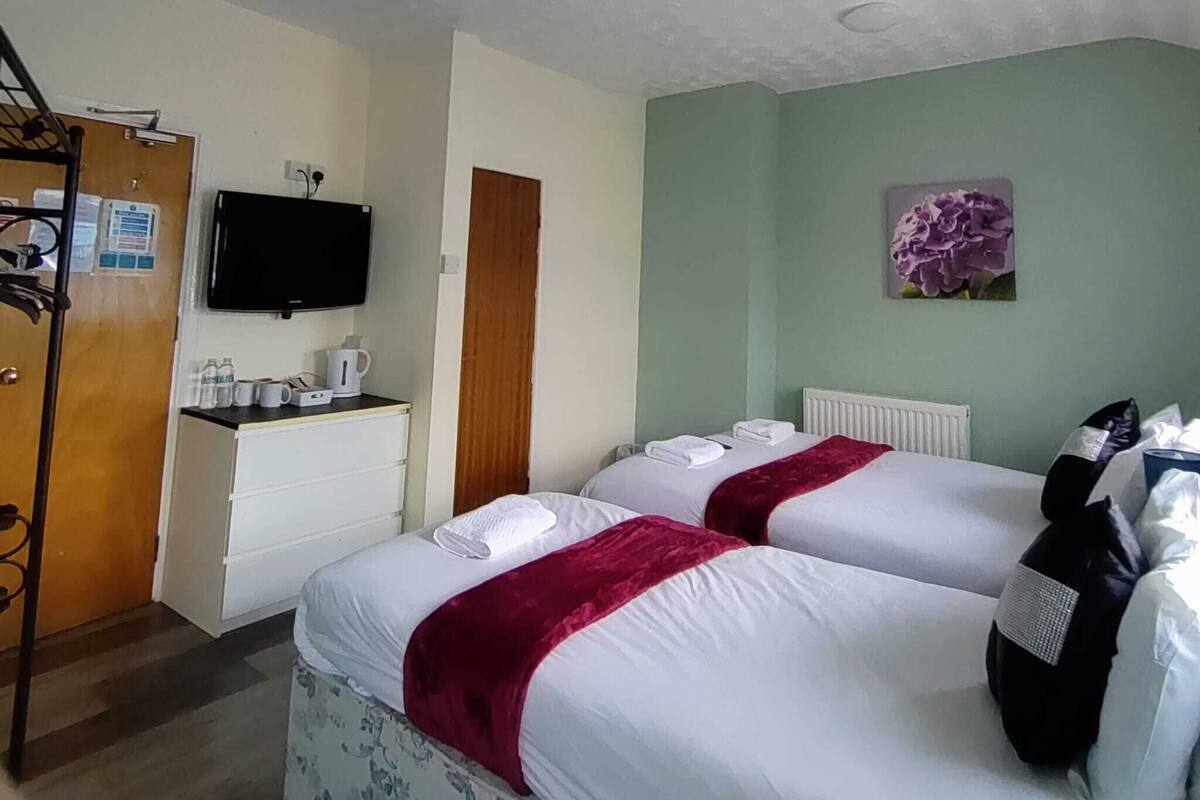 Une chambre d’hôtel avec deux lits, un bureau avec une machine à café, une télévision et une porte.