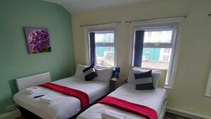 Une chambre avec deux lits, un radiateur, une fenêtre avec des rideaux et un tableau au mur.