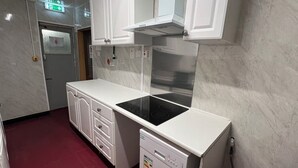 Une cuisine de taille réduite avec des meubles blancs, une cuisinière encastrée et un lave-vaisselle.