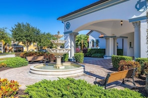 Une fontaine, des bancs et un bâtiment orné de colonnes et d’arcades.