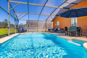 A swimming pool with a covered area, lounge chairs, and a table with chairs.