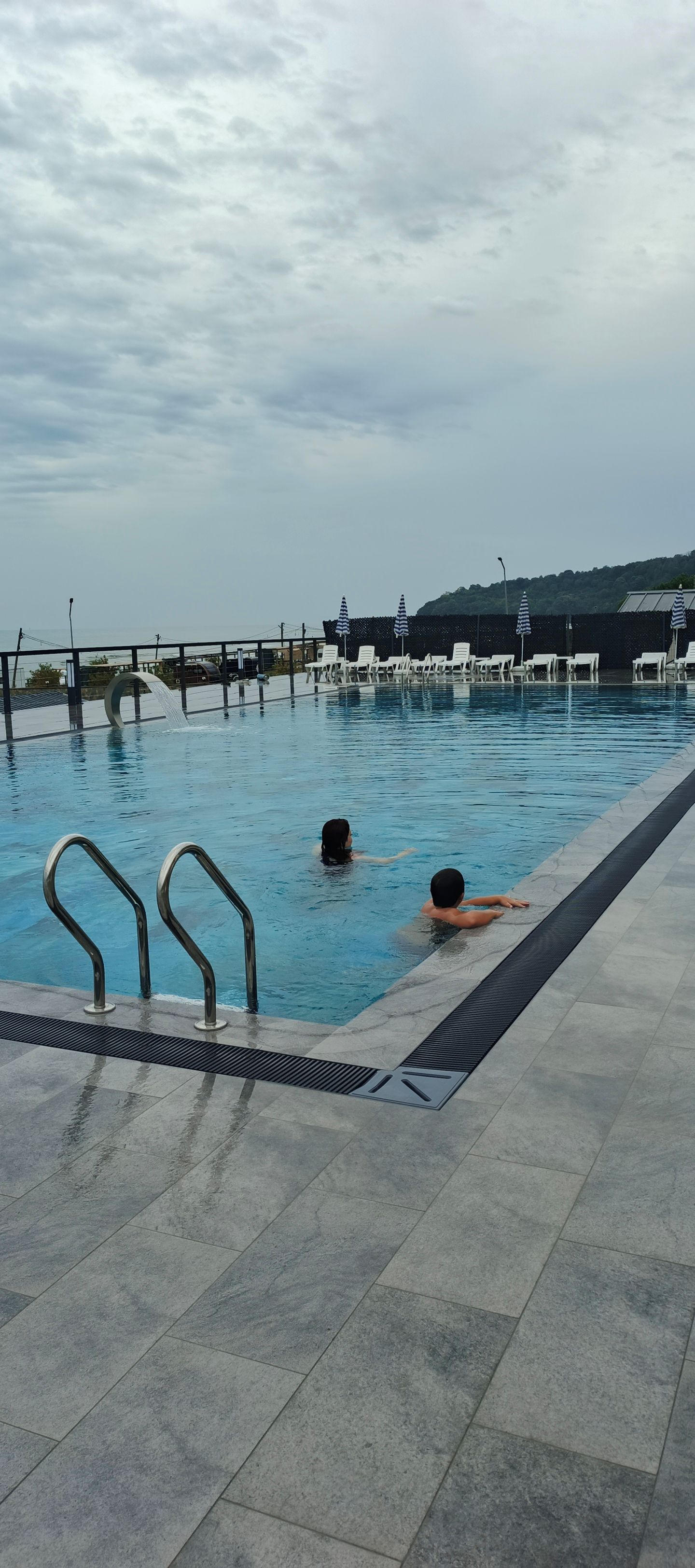 A swimming pool with a tiled deck, a metal ladder, and lounge chairs.
