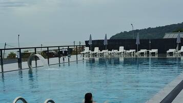 A swimming pool with a tiled deck, a metal ladder, and lounge chairs.
