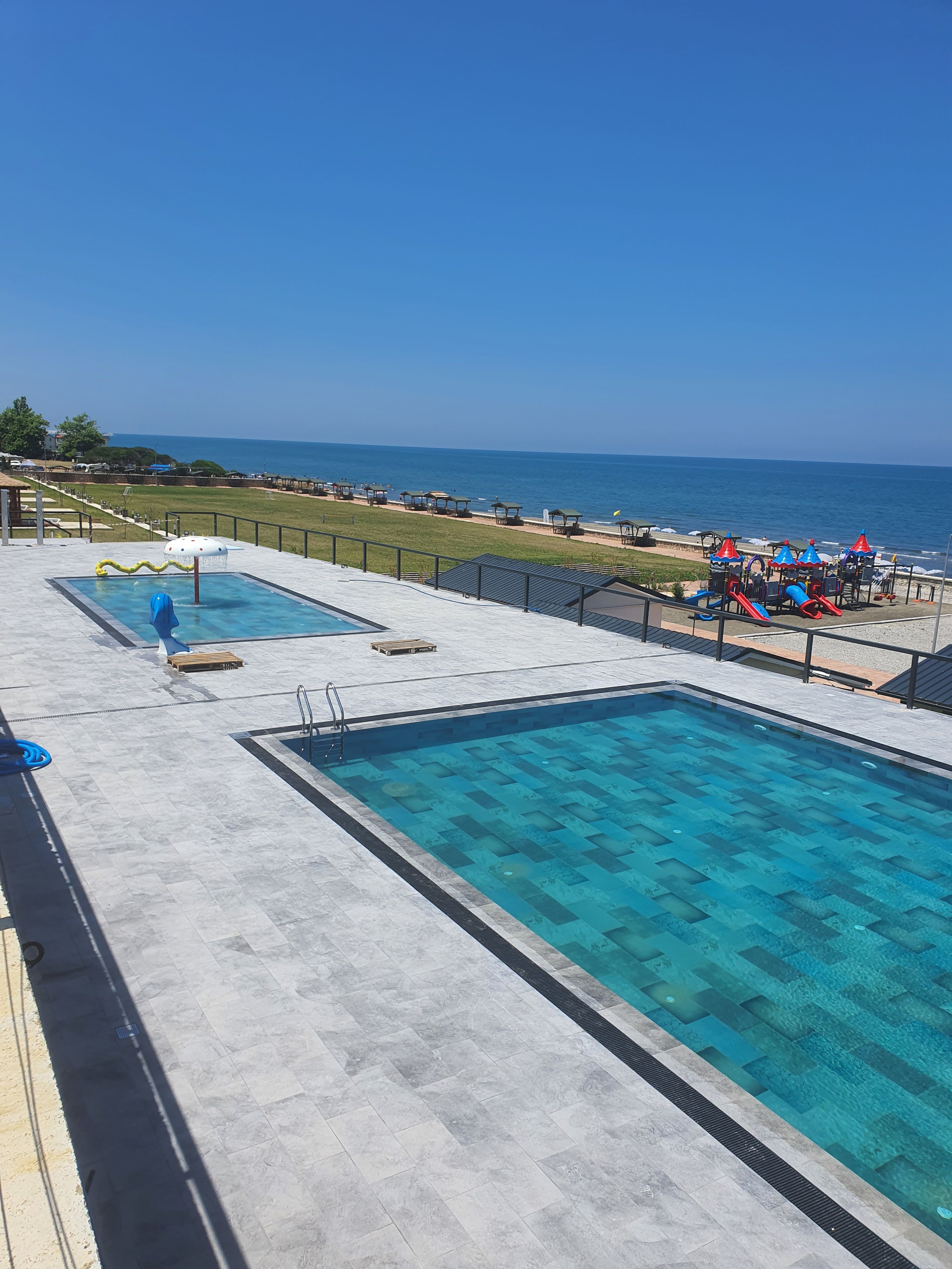 Ein Swimmingpool mit Meerblick, ein Kinderspielbereich und eine Rasenfläche mit Liegestühlen.