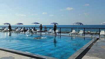 Una piscina con sillas de descanso y sombrillas, una terraza y vista al mar.